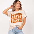 Woman wearing a sand Autumn Leaves and Pumpkins Please fall graphic tee with bold orange retro lettering.