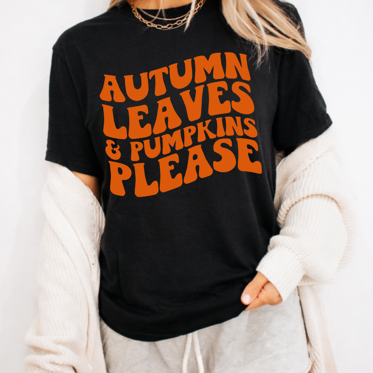 Woman wearing a black Autumn Leaves and Pumpkins Please fall graphic tee with bold orange retro lettering.