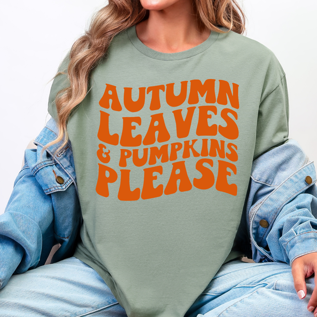 Woman wearing a sage Autumn Leaves and Pumpkins Please fall graphic tee with bold orange retro lettering.