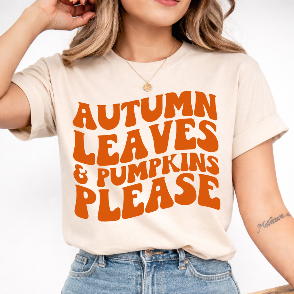 Woman wearing a sand Autumn Leaves and Pumpkins Please fall graphic tee with bold orange retro lettering.
