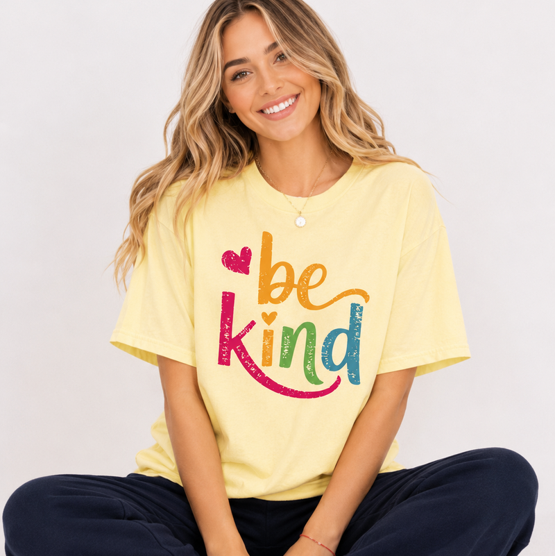 Woman wearing a yellow 'be kind' t-shirt sitting on the floor.