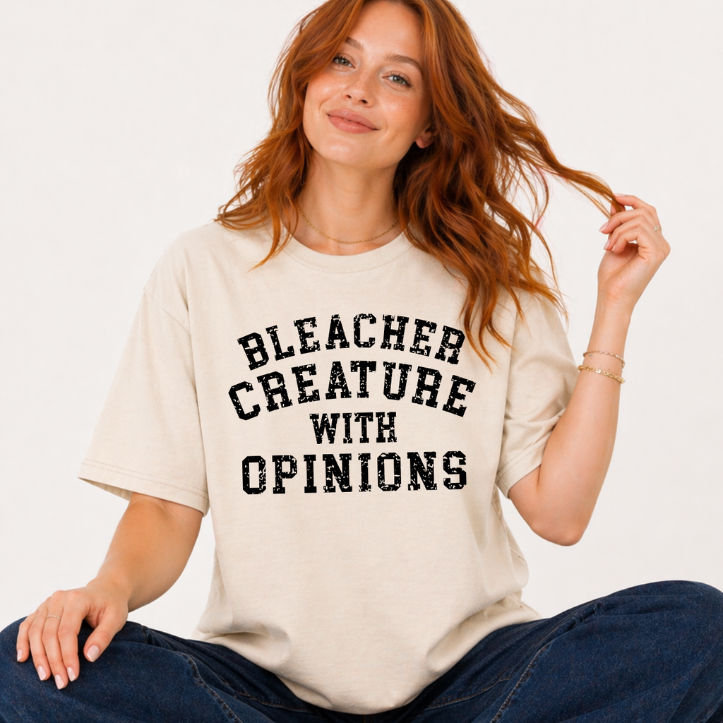 Woman wearing a beige t-shirt with 'BLEACHER CREATURE WITH OPINIONS' text.