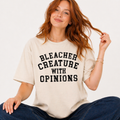 Woman wearing a beige t-shirt with 'BLEACHER CREATURE WITH OPINIONS' text.