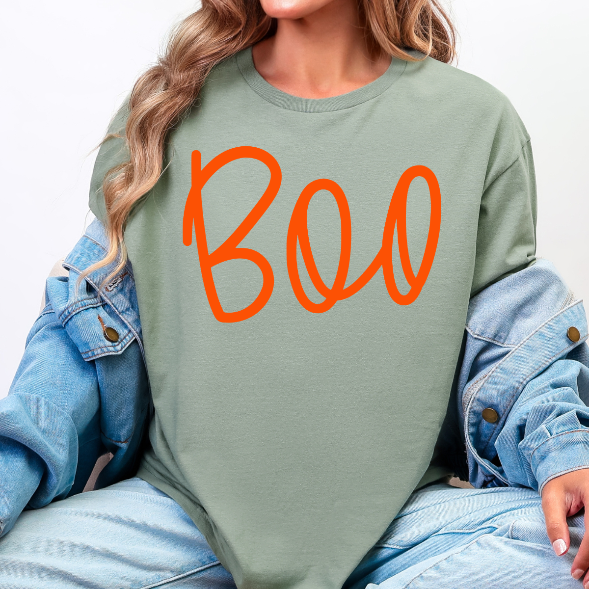 Woman wearing a sage Boo Halloween graphic tee with oversized orange script lettering.