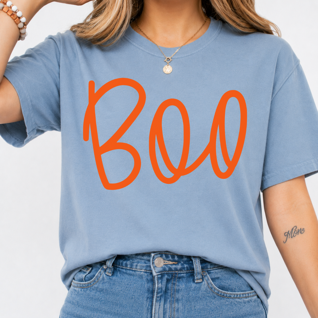 Woman wearing a stone blue Boo Halloween graphic tee with oversized orange script lettering.