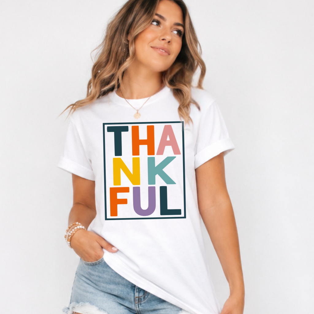 Woman wearing a white Thankful Thanksgiving graphic tee with colorful block lettering.