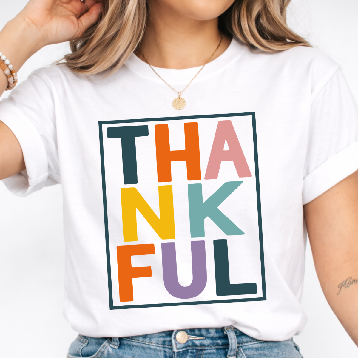 Woman wearing a white Thankful Thanksgiving graphic tee with colorful block lettering.