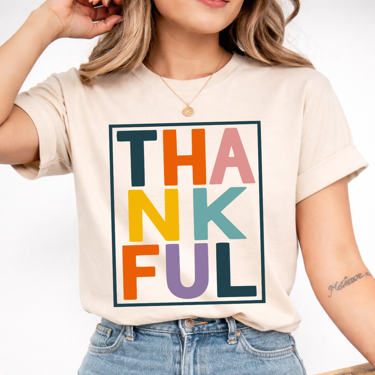 Woman wearing a sand Thankful Thanksgiving graphic tee with colorful block lettering.
