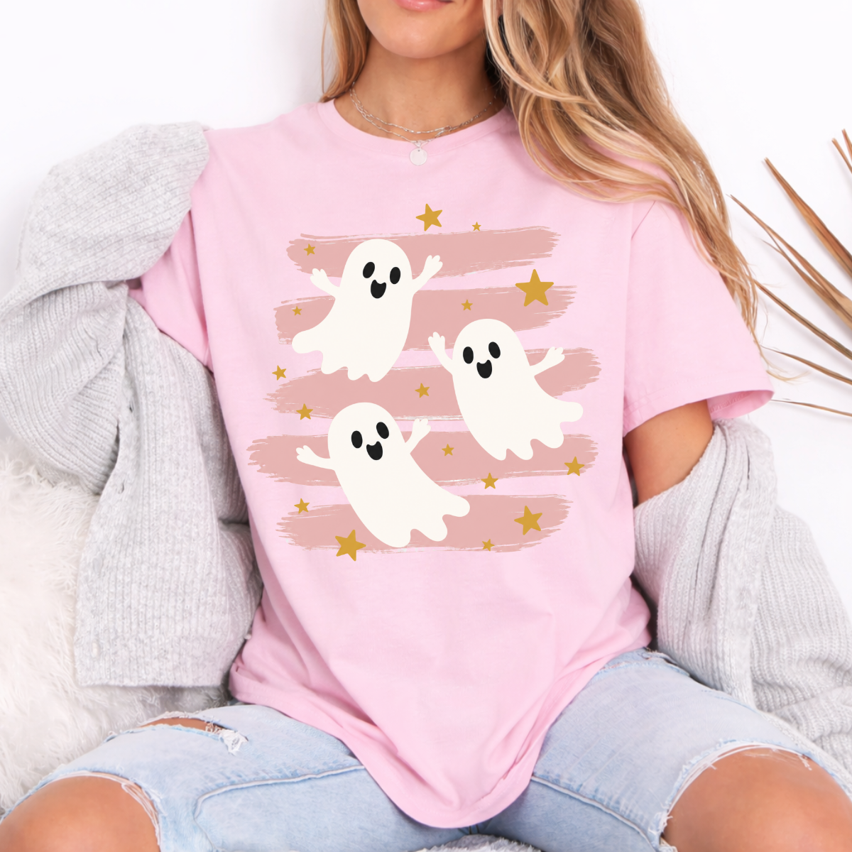 Woman wearing a light pink Halloween graphic tee with three white ghosts, pink brushstrokes, and gold stars.