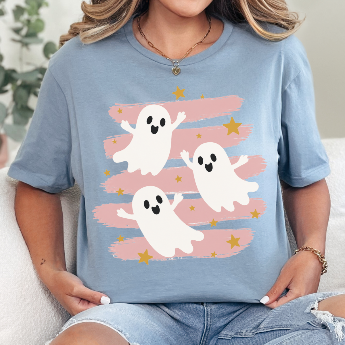 Woman wearing a stone blue Halloween graphic tee with three white ghosts, pink brushstrokes, and gold stars.