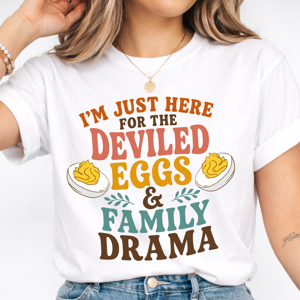 Woman wearing a white Deviled Eggs and Family Drama Thanksgiving graphic tee with colorful lettering and deviled egg illustrations.