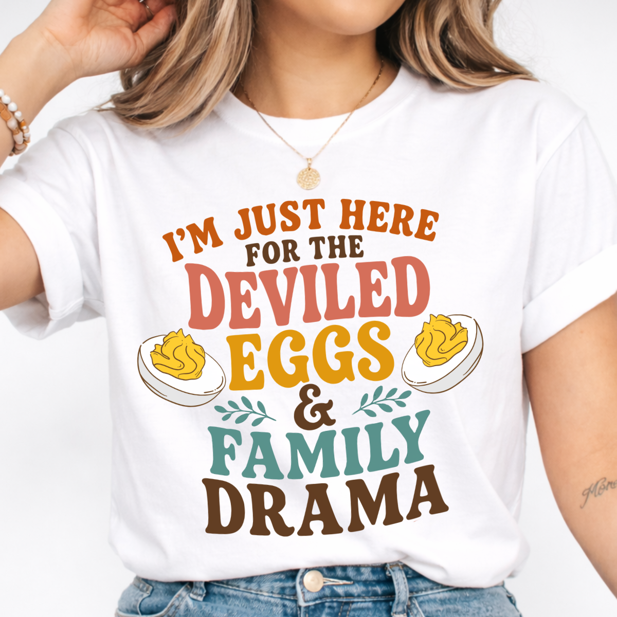 Woman wearing a white Deviled Eggs and Family Drama Thanksgiving graphic tee with colorful lettering and deviled egg illustrations.