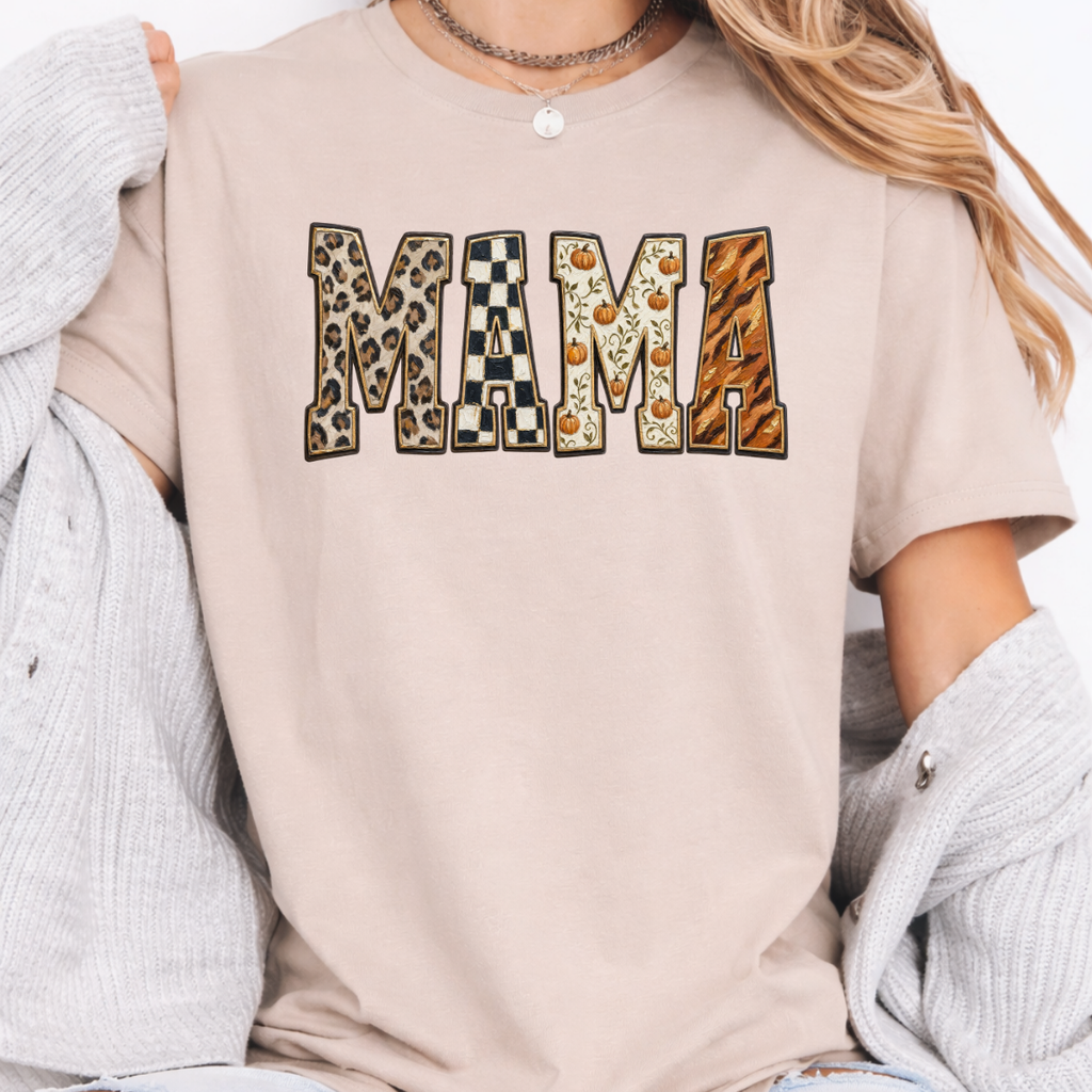Woman wearing a sand Fall Mama graphic tee with leopard print, checkerboard, pumpkin, and orange patterned lettering.