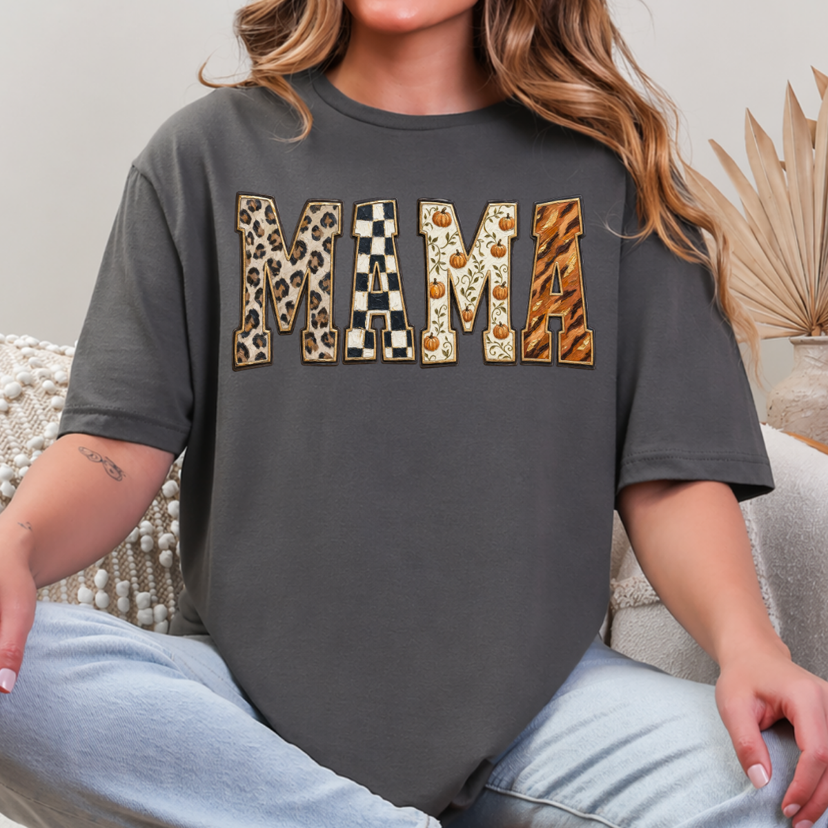Woman wearing a charcoal Fall Mama graphic tee with leopard print, checkerboard, pumpkin, and orange patterned lettering.