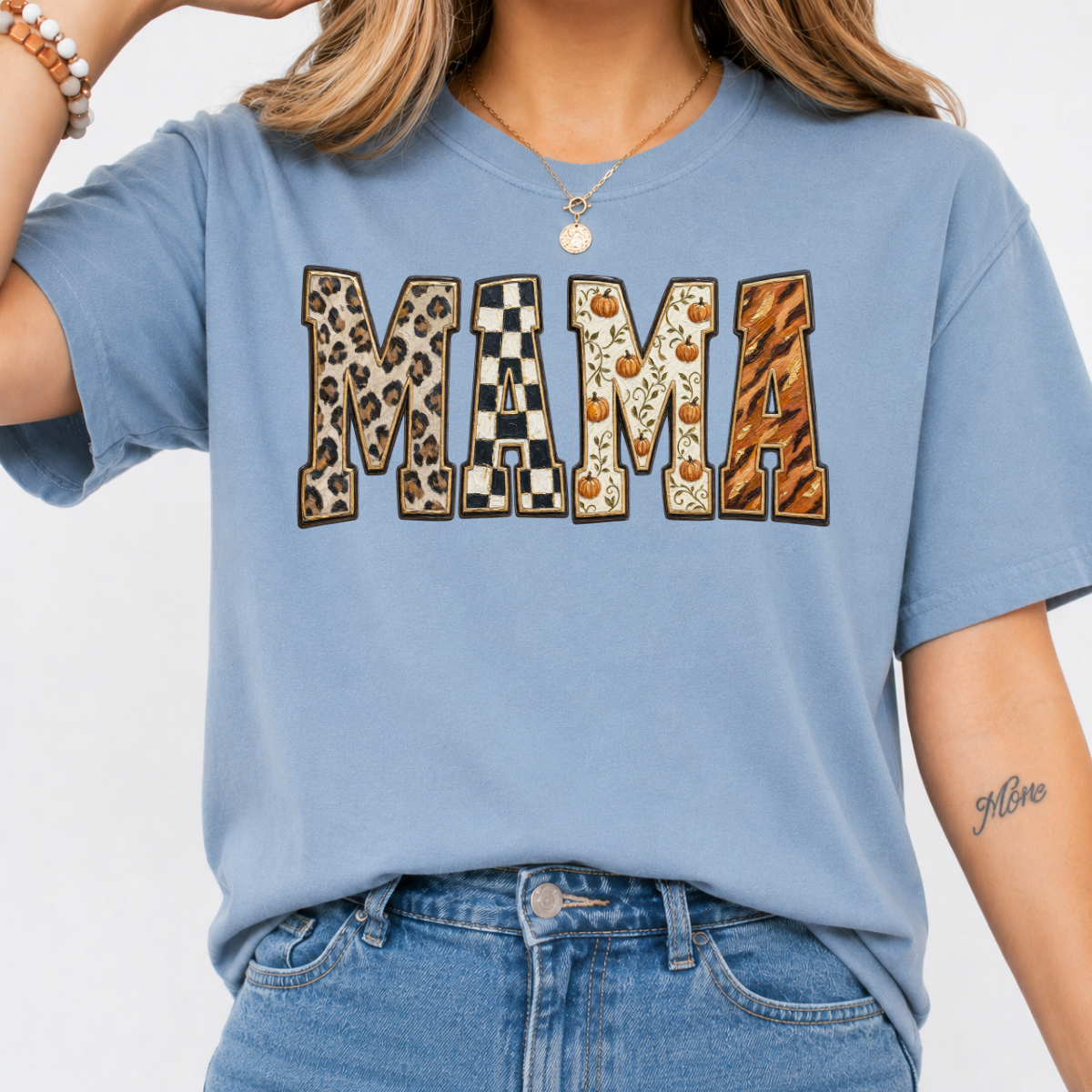 Woman wearing a stone blue Fall Mama graphic tee with leopard print, checkerboard, pumpkin, and orange patterned lettering.
