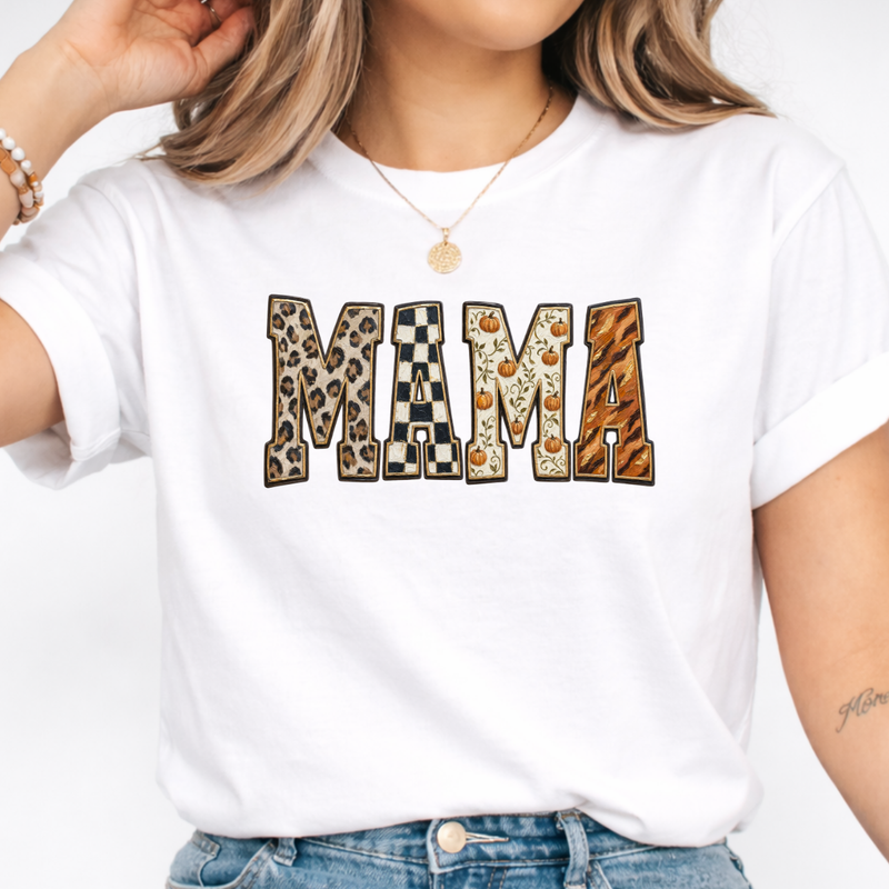 Woman wearing a white Fall Mama graphic tee with leopard print, checkerboard, pumpkin, and orange patterned lettering.