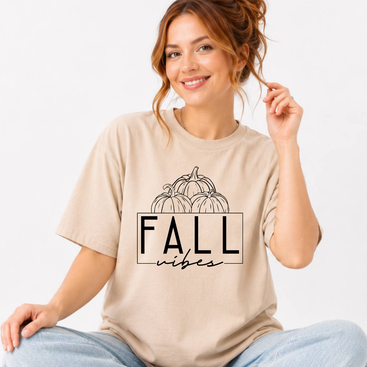 Woman wearing a sand Fall Vibes graphic tee with black pumpkin line art and minimalist lettering.