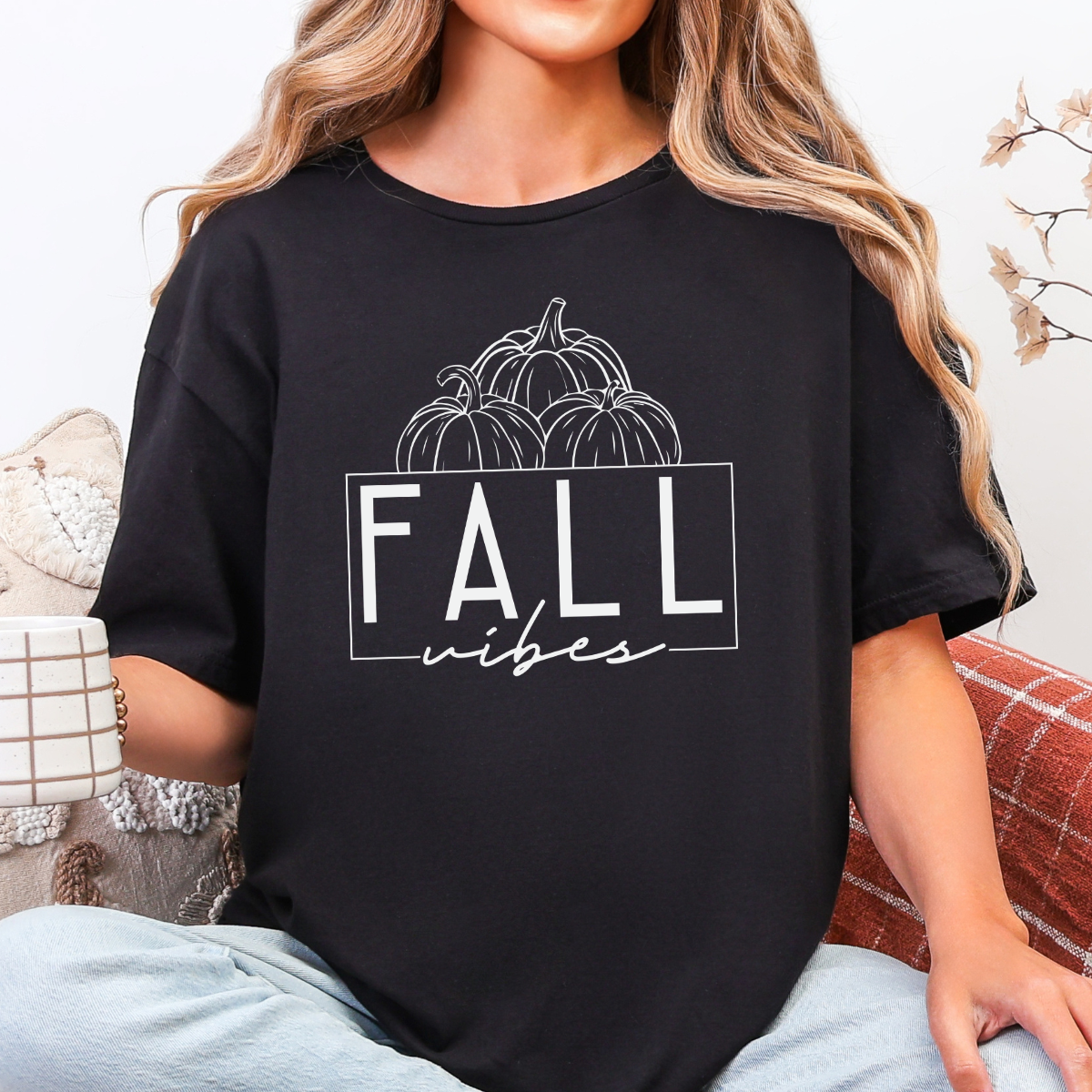Woman wearing a black Fall Vibes graphic tee with black pumpkin line art and minimalist lettering.