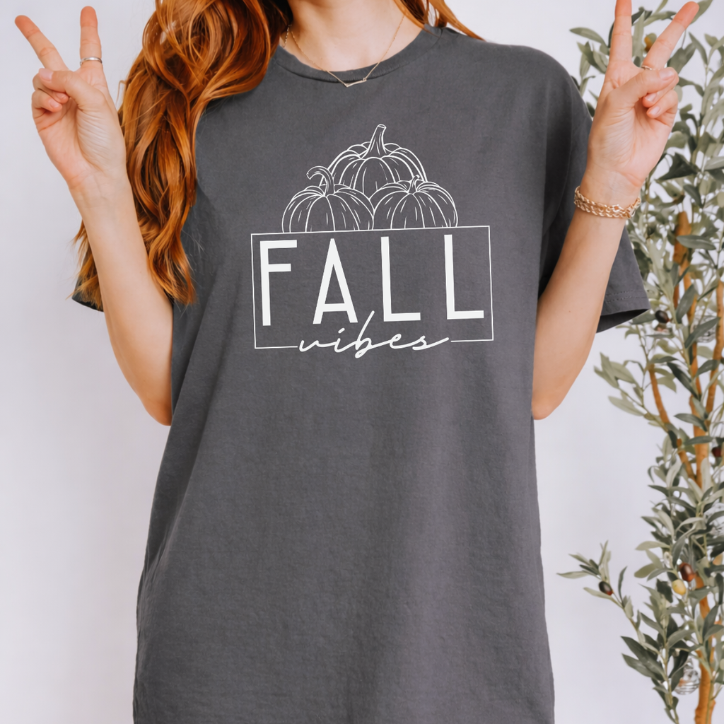 Woman wearing a charcoal Fall Vibes graphic tee with black pumpkin line art and minimalist lettering.