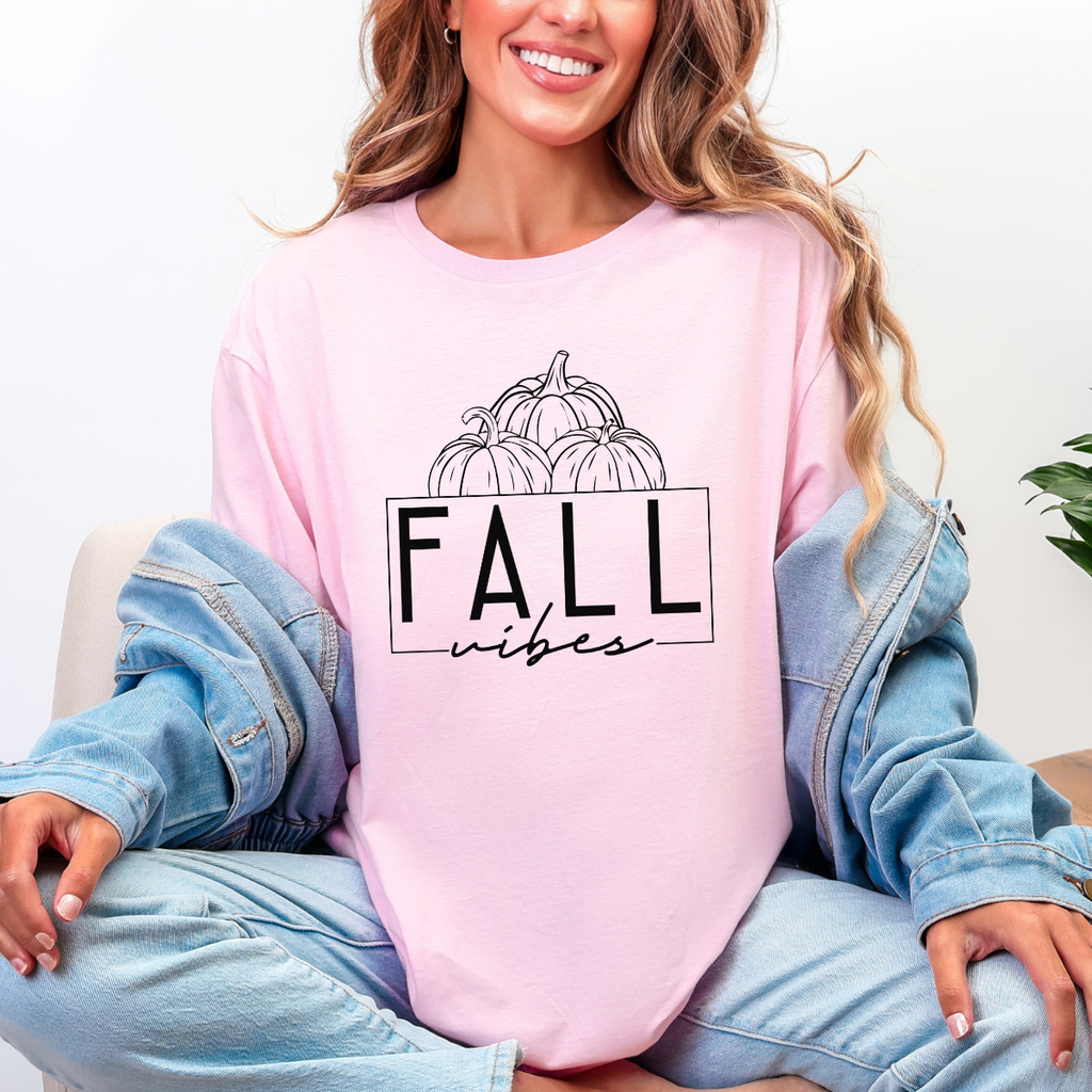 Woman wearing a light pink Fall Vibes graphic tee with black pumpkin line art and minimalist lettering.