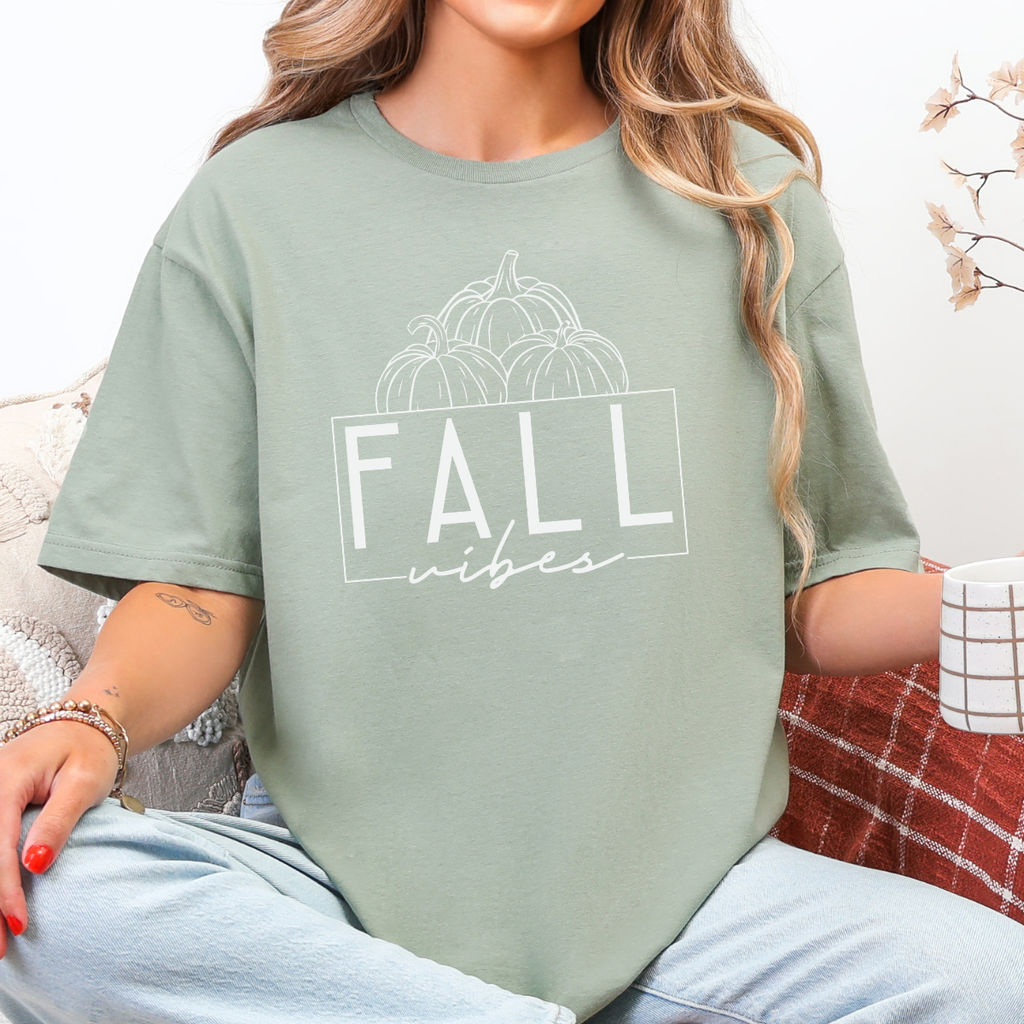 Woman wearing a sage Fall Vibes graphic tee with black pumpkin line art and minimalist lettering.