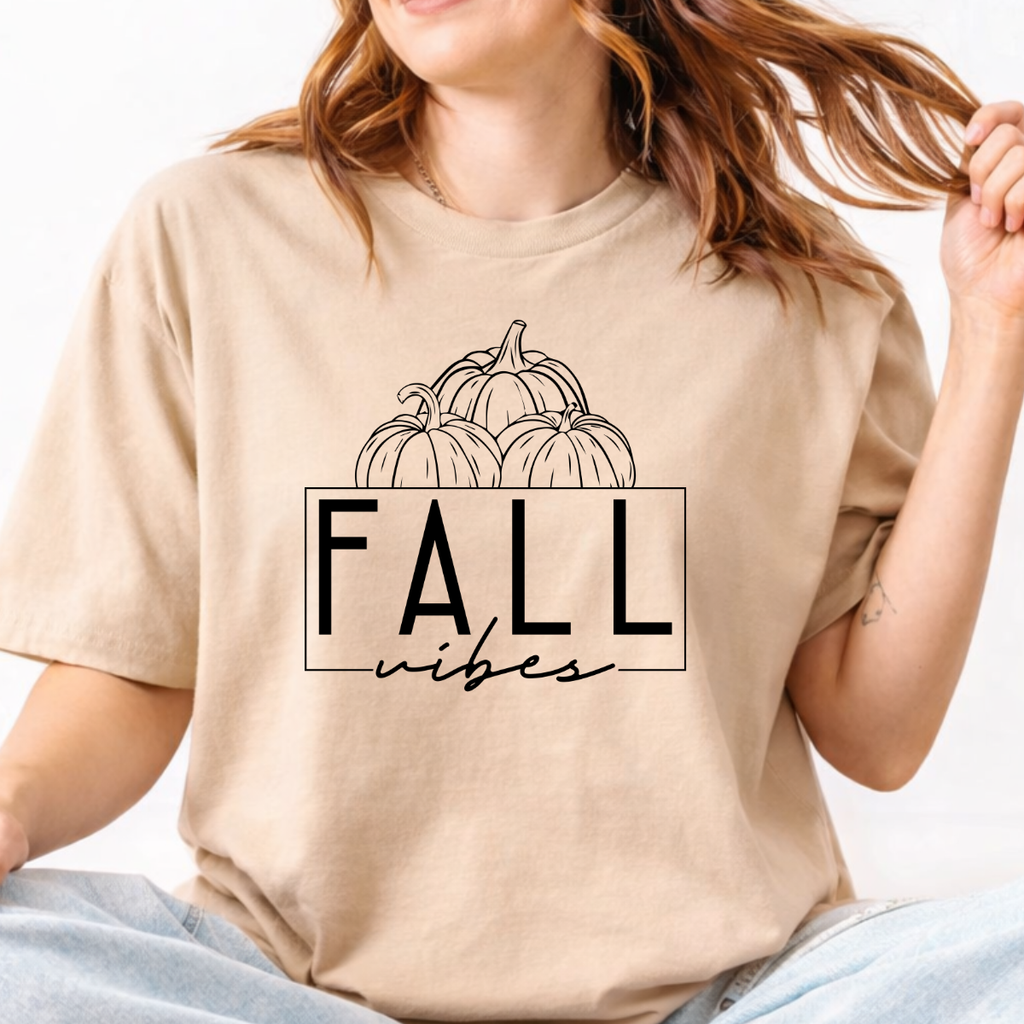 Woman wearing a sand Fall Vibes graphic tee with black pumpkin line art and minimalist lettering.