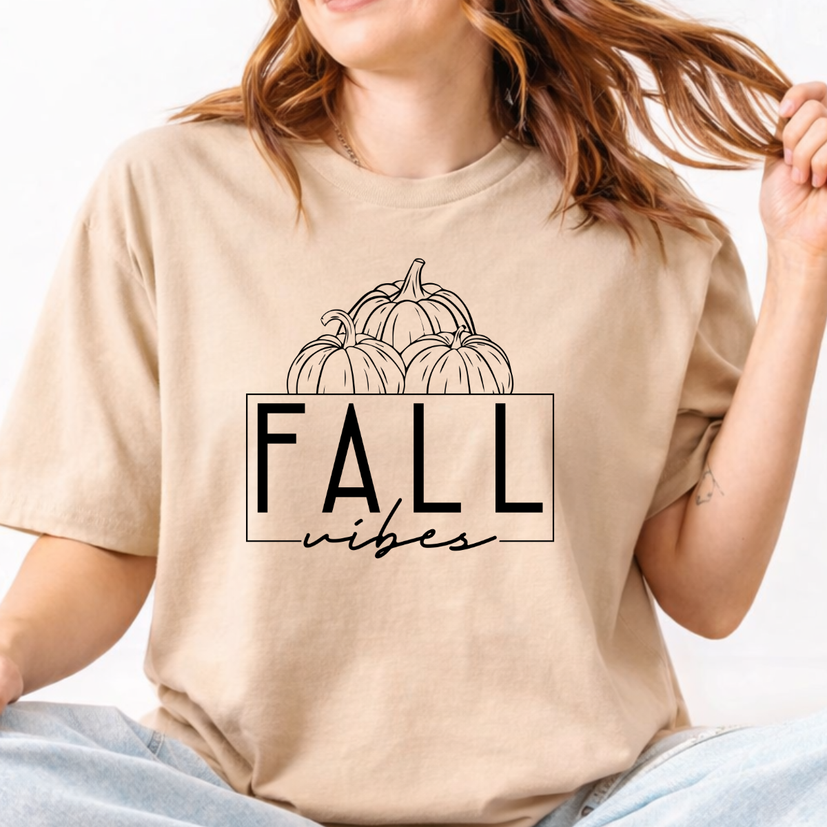 Woman wearing a sand Fall Vibes graphic tee with black pumpkin line art and minimalist lettering.