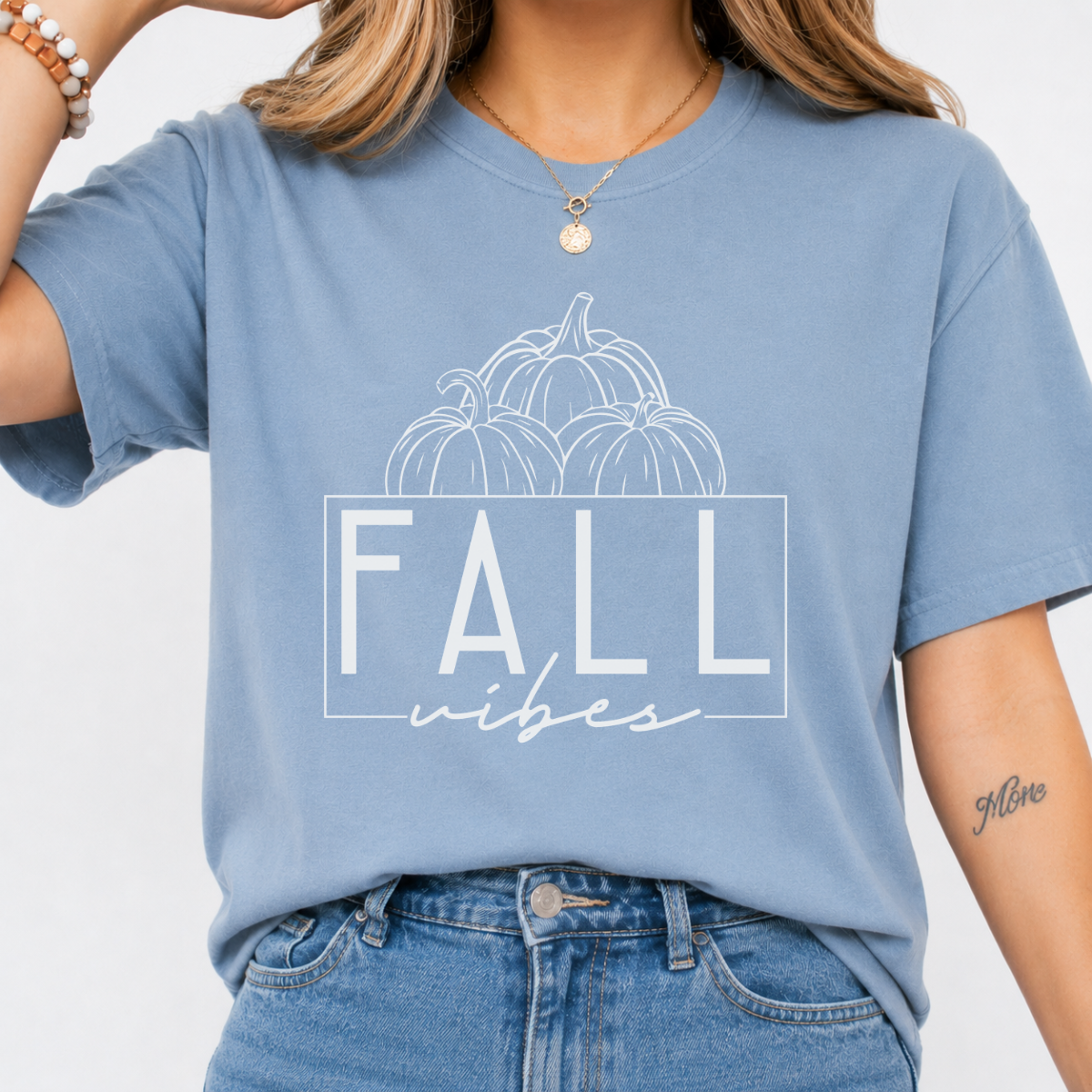 Woman wearing a stone blue Fall Vibes graphic tee with black pumpkin line art and minimalist lettering.