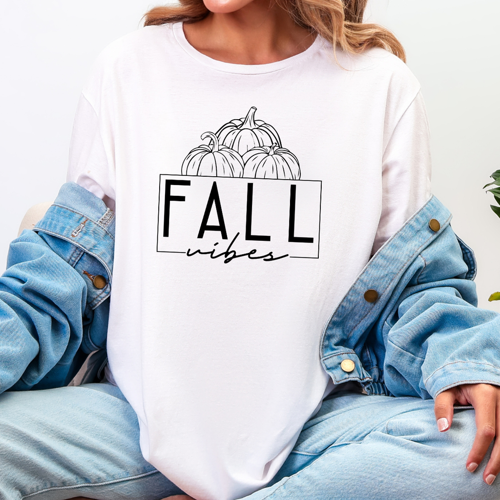 Woman wearing a white Fall Vibes graphic tee with black pumpkin line art and minimalist lettering.