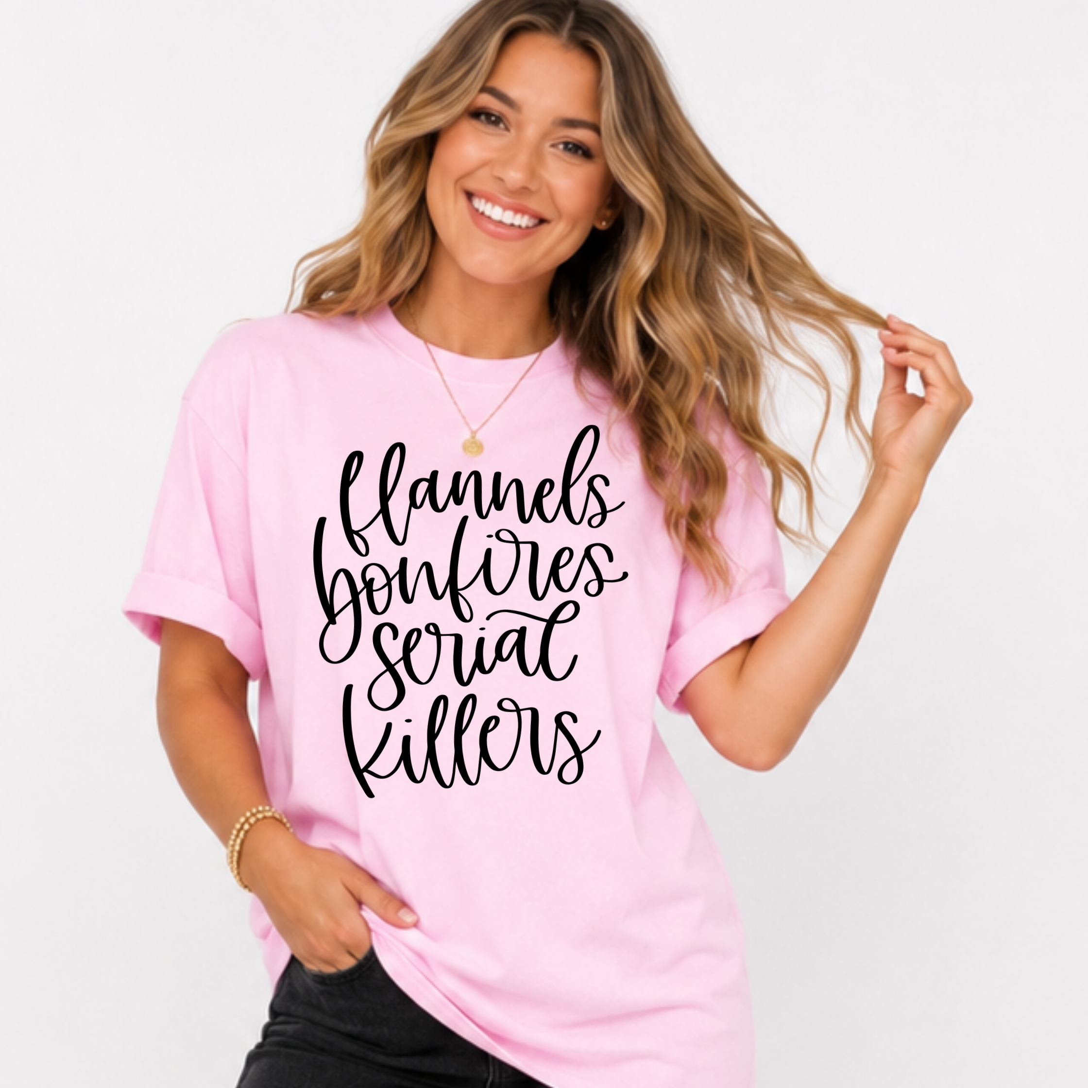 Woman wearing a light pink Flannels Bonfires and Serial Killers fall graphic tee with black script lettering.