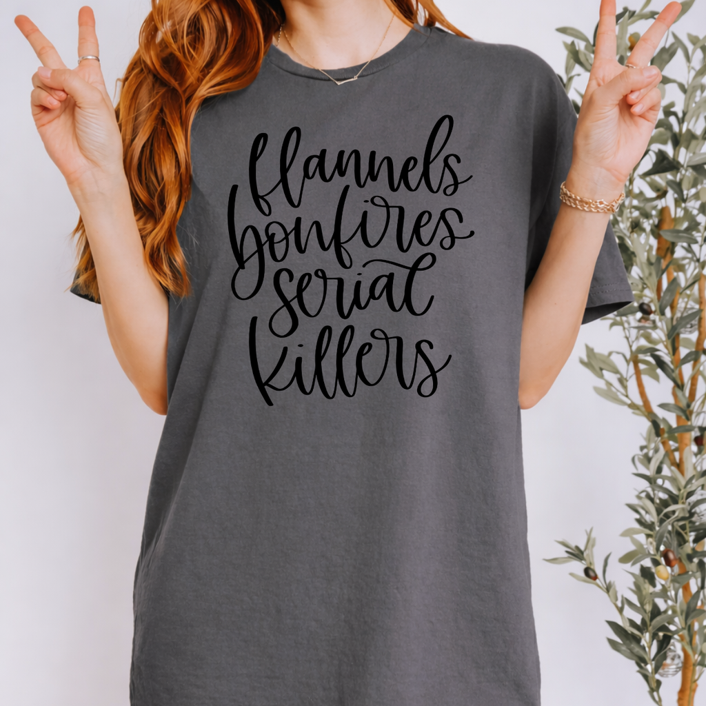Woman wearing a charcoal Flannels Bonfires and Serial Killers fall graphic tee with black script lettering.