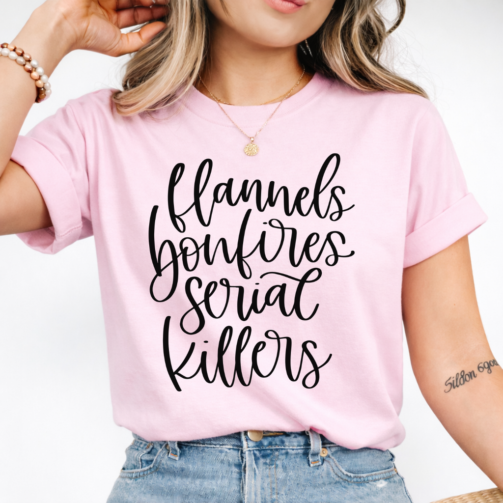 Woman wearing a light pink Flannels Bonfires and Serial Killers fall graphic tee with black script lettering.