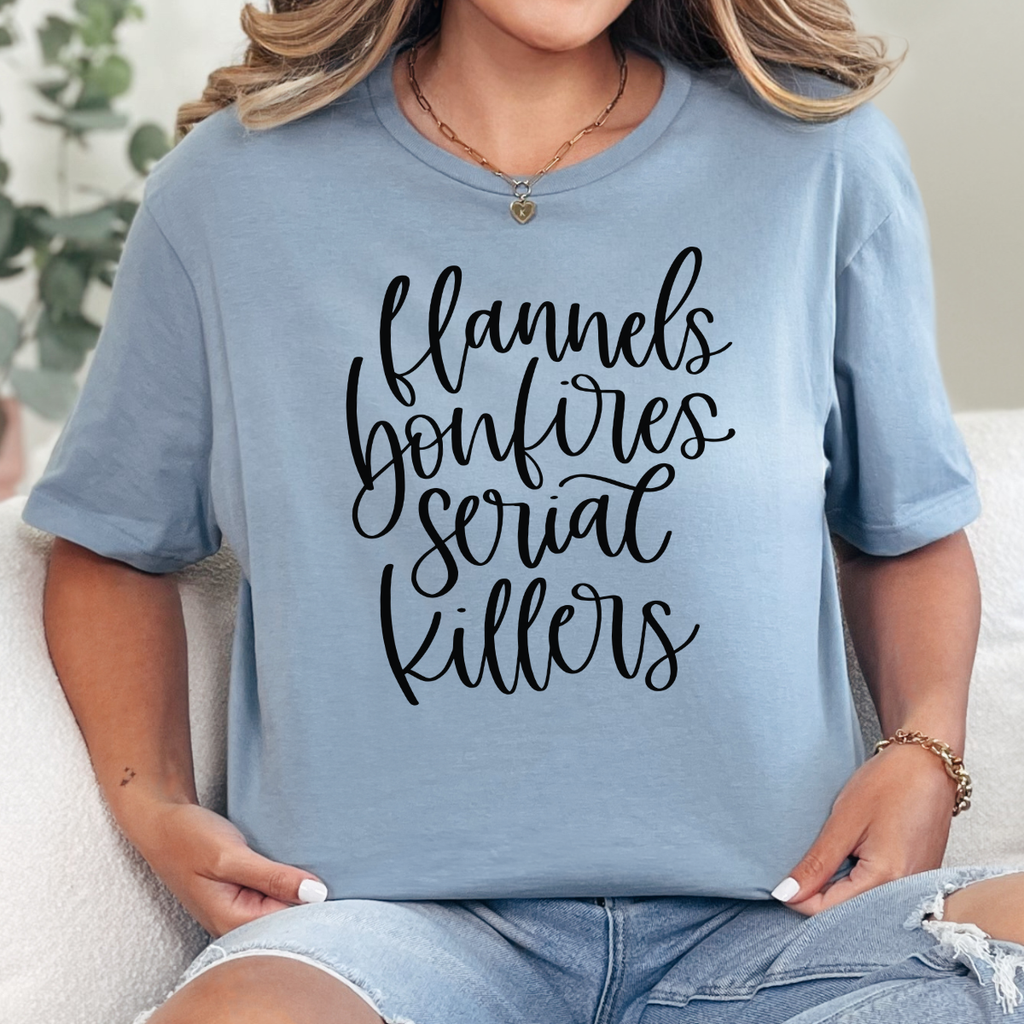 Woman wearing a stone blue Flannels Bonfires and Serial Killers fall graphic tee with black script lettering.