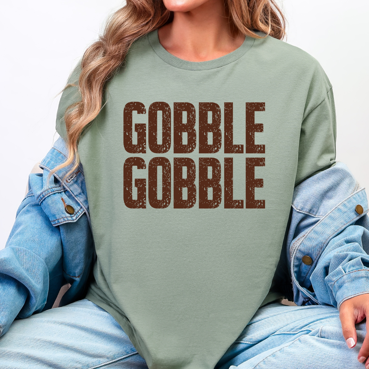 Woman wearing a sage Gobble Gobble Thanksgiving graphic tee with distressed brown lettering.