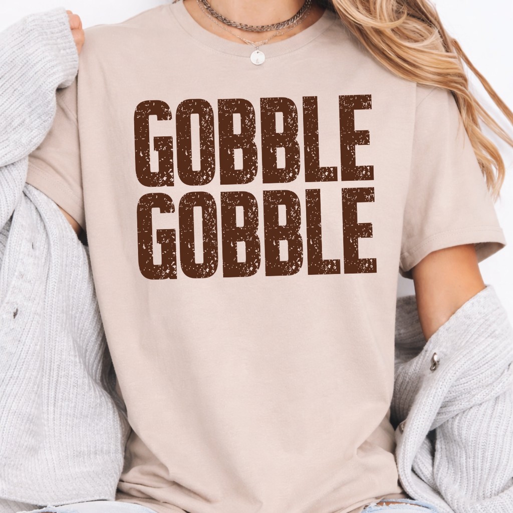 Woman wearing a sand Gobble Gobble Thanksgiving graphic tee with distressed brown lettering.