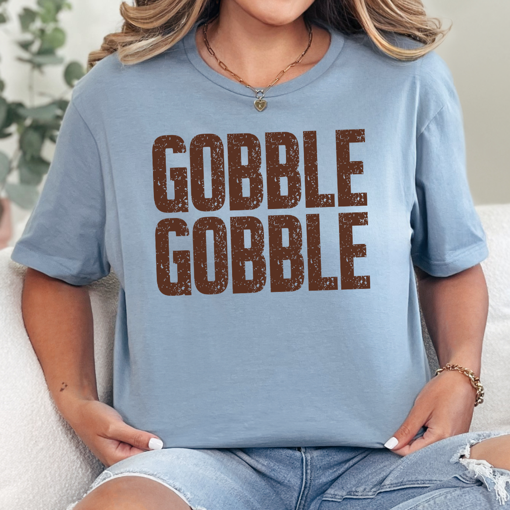 Woman wearing a stone blue Gobble Gobble Thanksgiving graphic tee with distressed brown lettering.