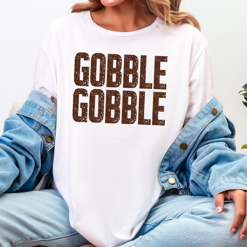 Woman wearing a white Gobble Gobble Thanksgiving graphic tee with distressed brown lettering.