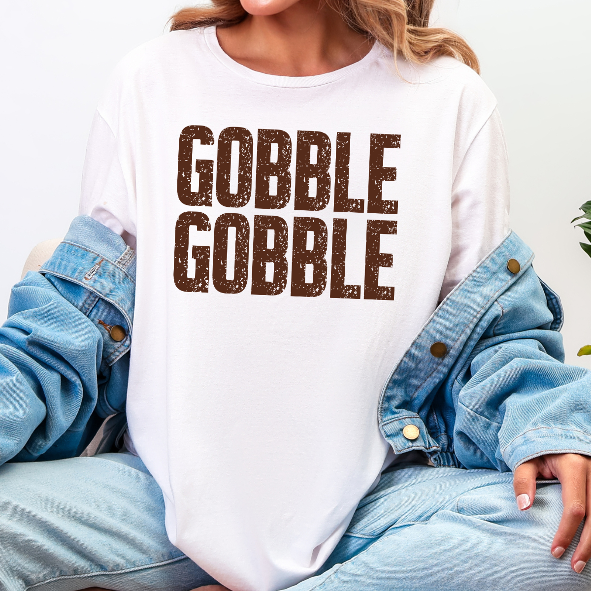 Woman wearing a white Gobble Gobble Thanksgiving graphic tee with distressed brown lettering.