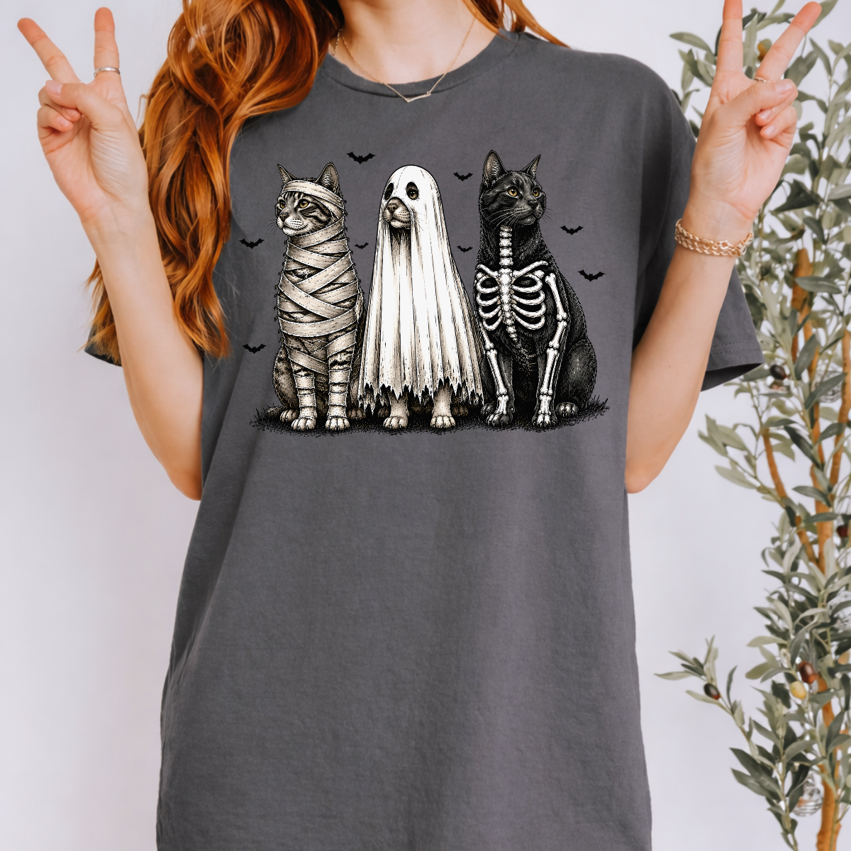 Woman wearing a charcoal Halloween cats graphic tee with mummy, ghost, and skeleton cats