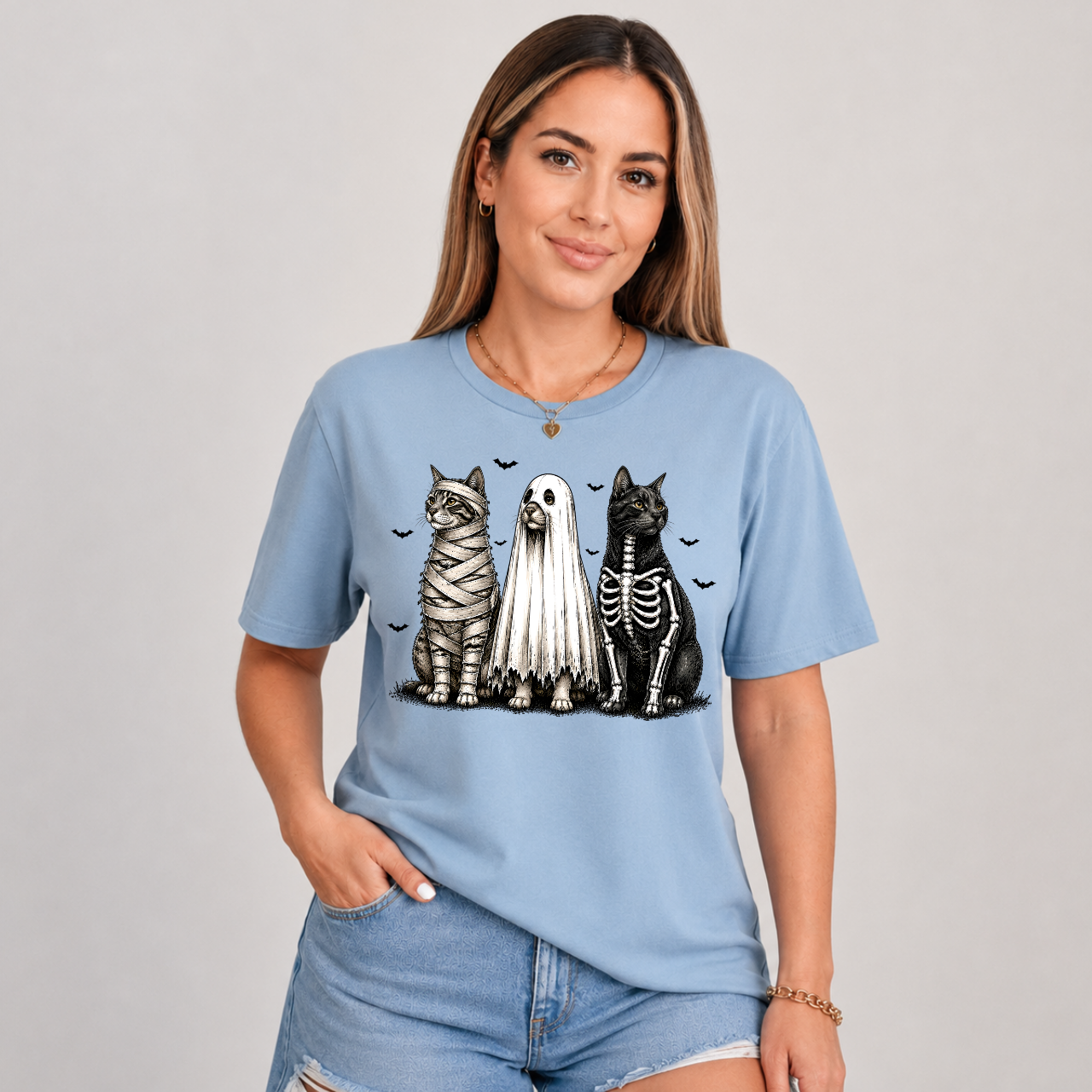 Woman wearing a sage green Halloween cats graphic tee with mummy, ghost, and skeleton cats