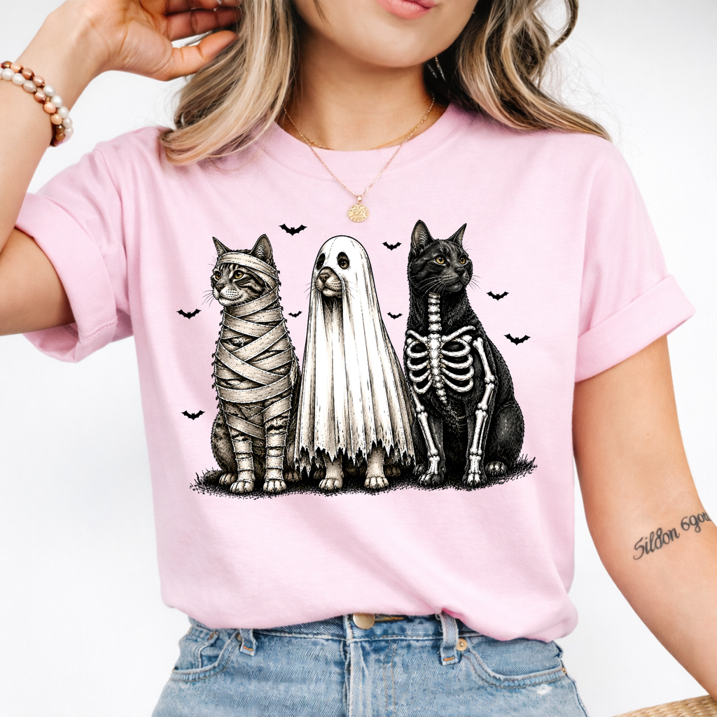 Woman wearing a light pink Halloween cats graphic tee with mummy, ghost, and skeleton cats