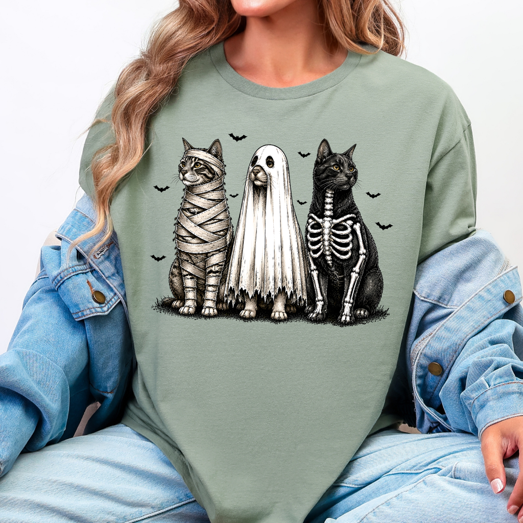 Woman wearing a sage green Halloween cats graphic tee with mummy, ghost, and skeleton cats
