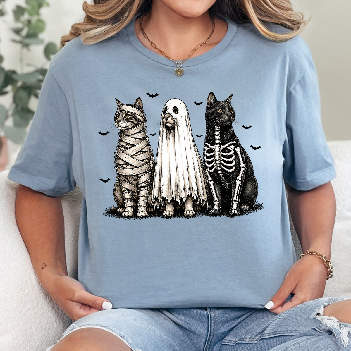 Woman wearing a stone blue Halloween cats graphic tee with mummy, ghost, and skeleton cats
