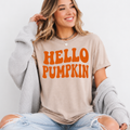 Woman wearing a sand Hello Pumpkin fall graphic tee with bold orange retro lettering.
