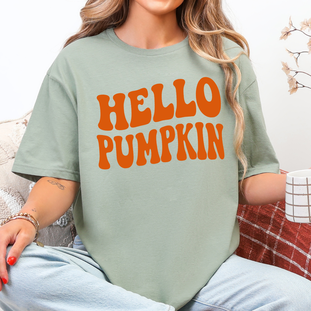 Woman wearing a sage Hello Pumpkin fall graphic tee with bold orange retro lettering.