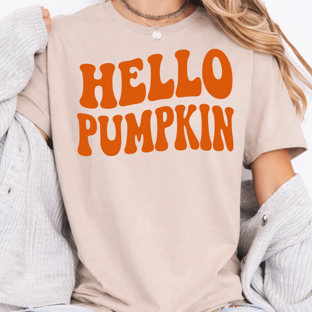 Woman wearing a sand Hello Pumpkin fall graphic tee with bold orange retro lettering.
