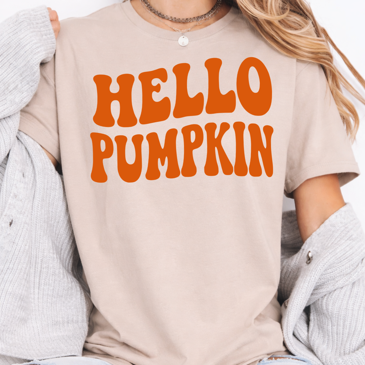 Woman wearing a sand Hello Pumpkin fall graphic tee with bold orange retro lettering.