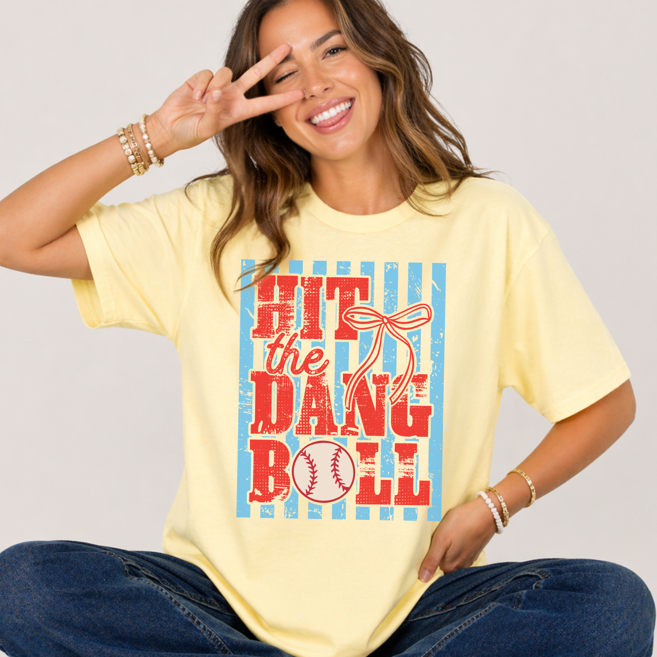 Woman wearing a yellow t-shirt with a colorful graphic and text that says 'Hit the Dang Ball'.
