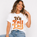 Woman wearing a white It’s Fall Y’all graphic tee with brown and orange retro lettering.