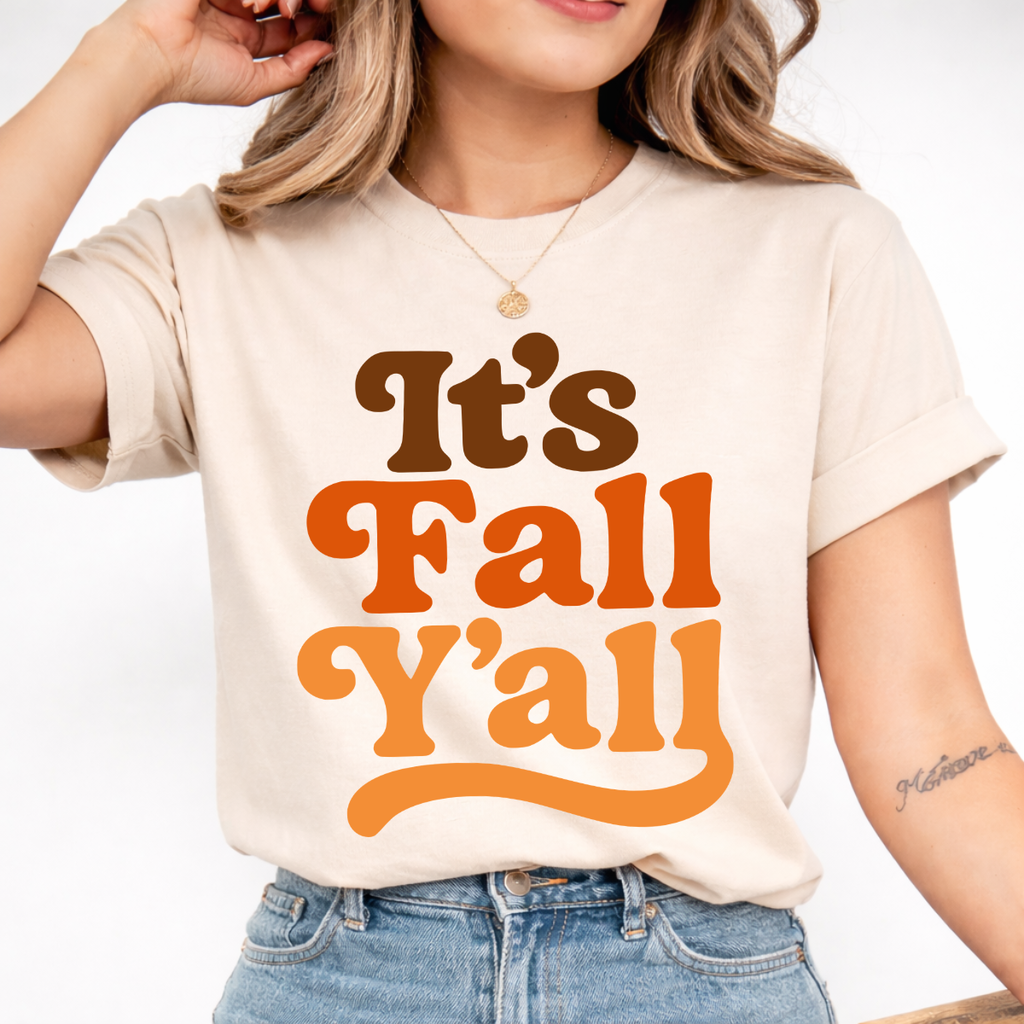 Woman wearing a sand It’s Fall Y’all graphic tee with brown and orange retro lettering.